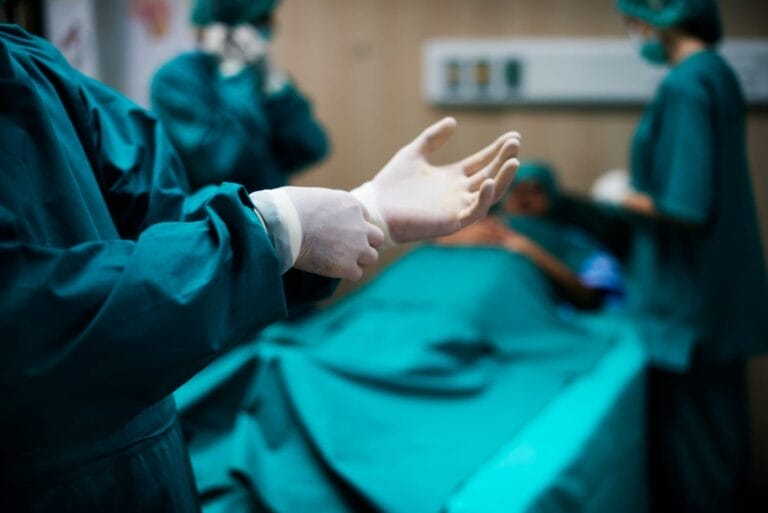 Dokter mengenakan sarung tangan bedah sebelum melakukan operasi pada pasien di ruang operasi.