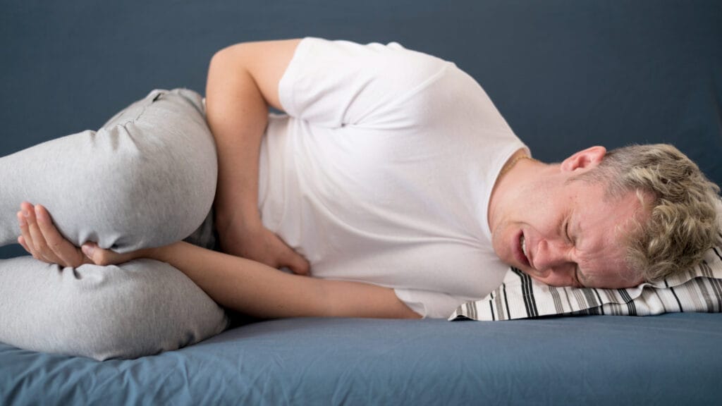 Pria berbaring kesakitan sambil memegang perut bagian bawah, menunjukkan gejala nyeri akibat infeksi saluran kemih atau uretritis gonore.