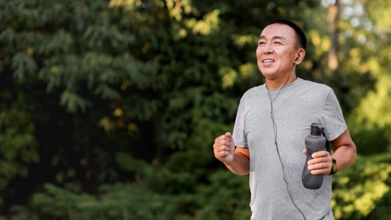 Pria paruh baya sedang jogging di taman sambil membawa botol air minum, menunjukkan gaya hidup sehat untuk menjaga kesehatan ginjal