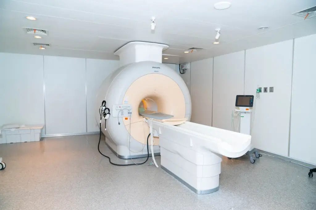 Mesin MRI di ruang medis yang bersih dan terang dengan peralatan kontrol di dekatnya, mendukung diagnosis yang akurat dan pengobatan batu ginjal.