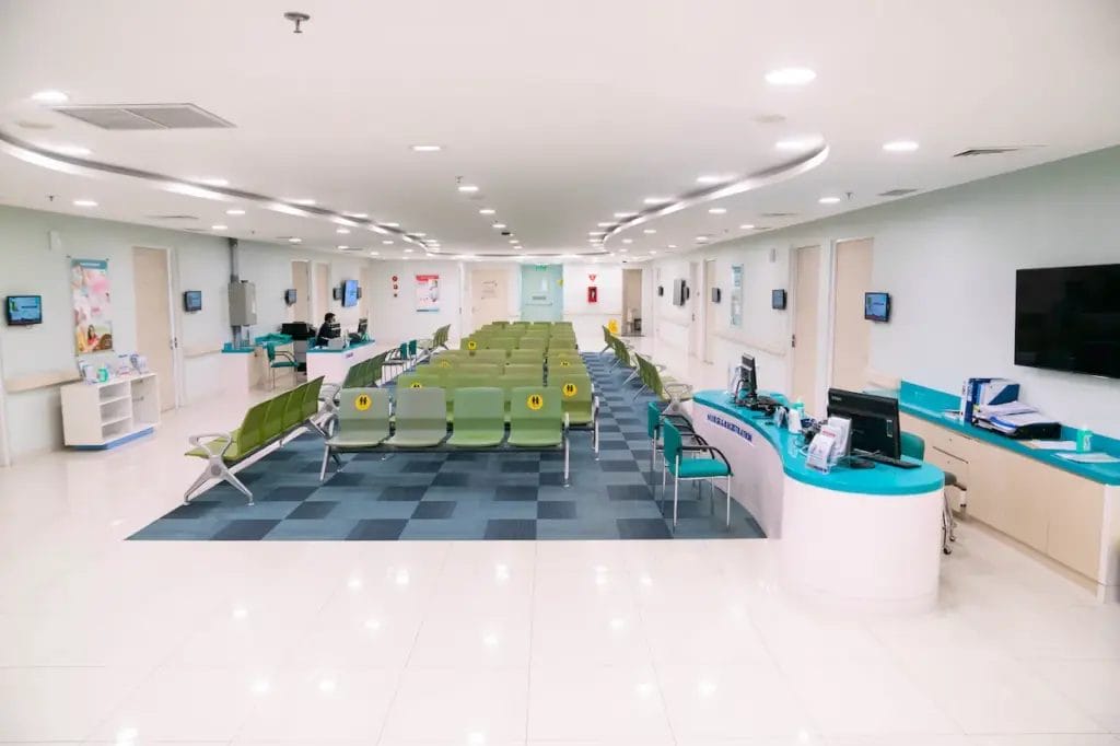 Ruang tunggu rumah sakit modern dengan deretan kursi hijau, meja resepsionis, dan pencahayaan yang terang, dirancang untuk pasien yang mencari pengobatan batu ginjal di lingkungan yang nyaman.