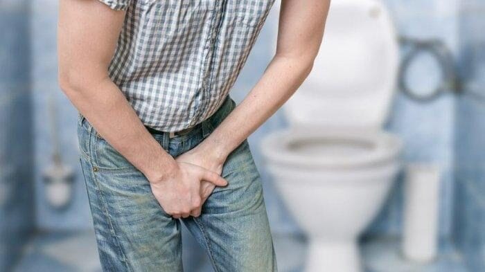 Seseorang berdiri di depan toilet, memegang perut bagian bawah dan area selangkangannya, yang mungkin mengindikasikan ketidaknyamanan atau keinginan untuk buang air kecil sebuah skenario yang ideal untuk mengilustrasikan Konsep Otomatis dalam solusi toilet.